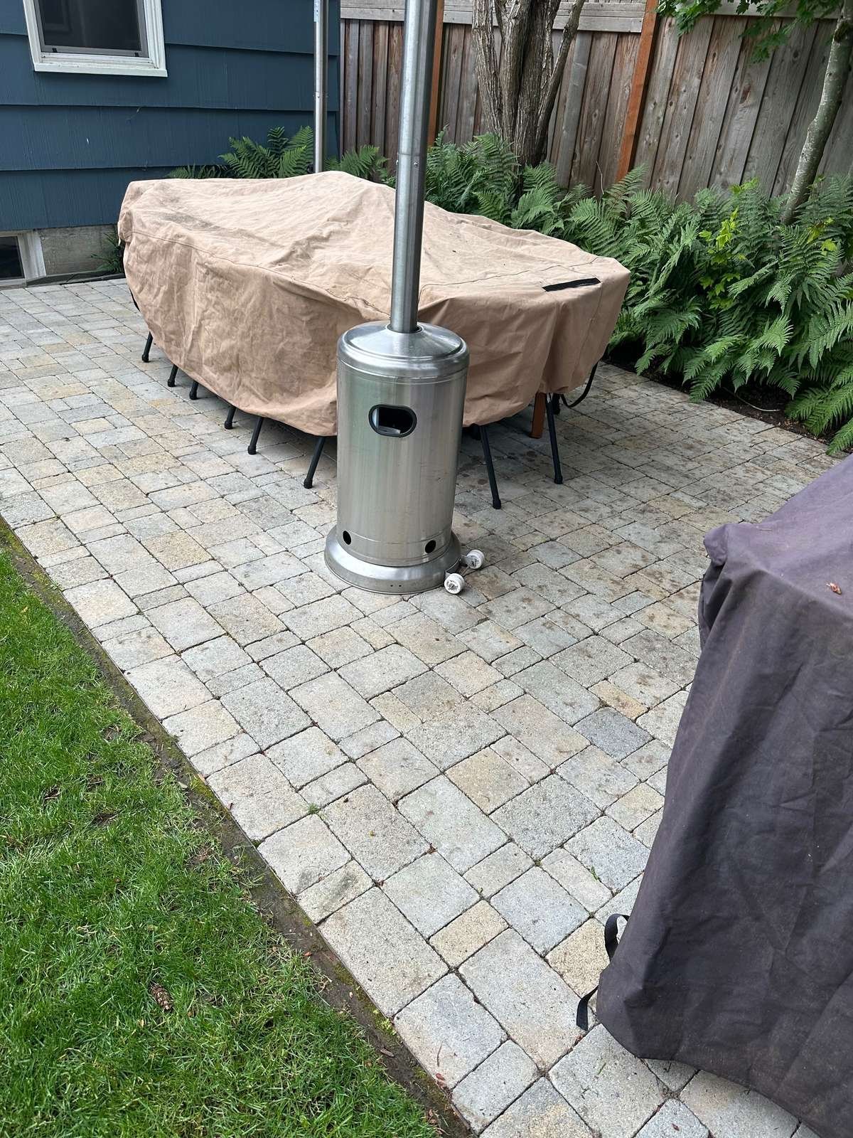 Struver-built paver patio with covered outdoor dining furniture and a tall stainless heater, edged cleanly to lawn with a wood fence behind